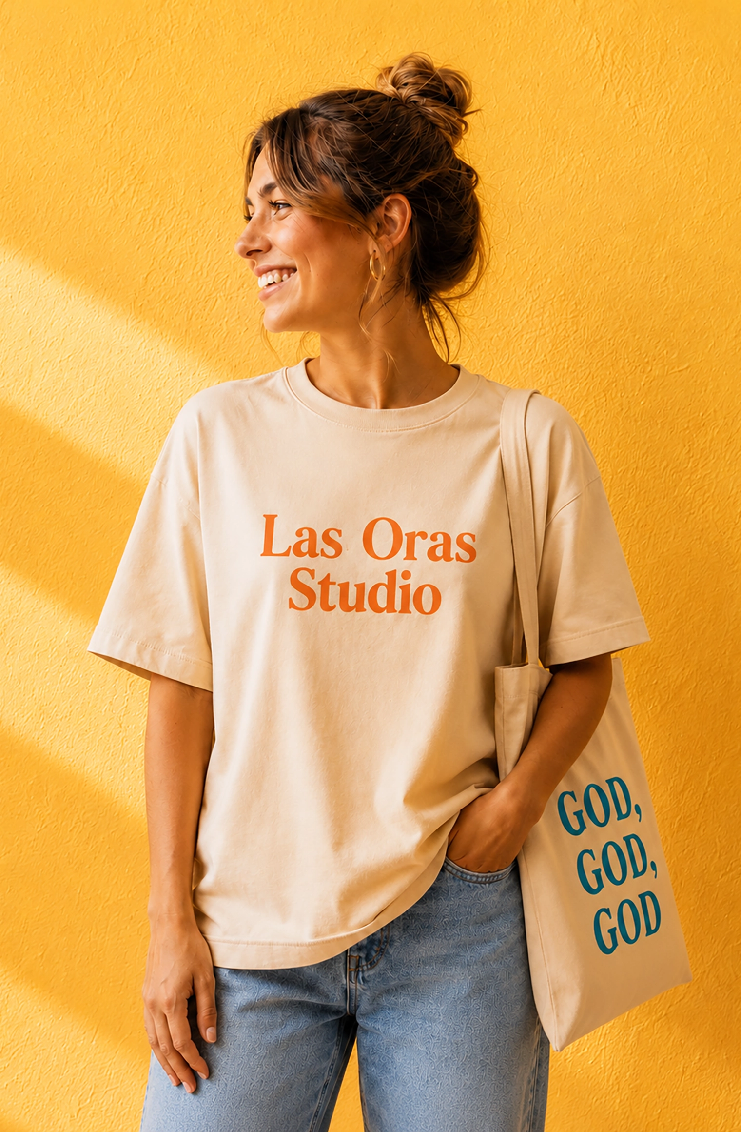 Mujer sonriente con camiseta y bolsa personalizadas de Las Oras Studio ante una pared amarilla